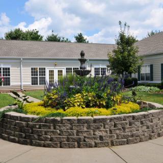 A beautifully landscaped garden with a central fountain in front of a building.