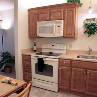 A compact kitchen with wooden cabinets, an oven, a microwave, and a sink.