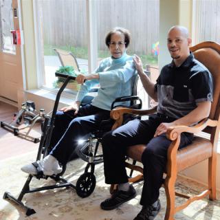 Two seniors engage in a physical therapy session indoors, using an exercise machine aimed at rehabilitation.