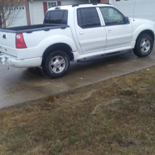 A white pickup truck parked on a wet driveway next to a grassy area.