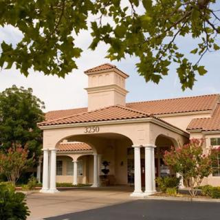 A scenic view of a building entrance with columns and a tiled roof surrounded by trees.