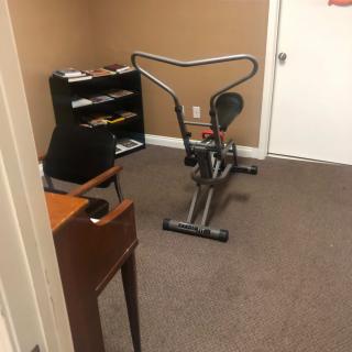 An office space with an exercise bike and desk.