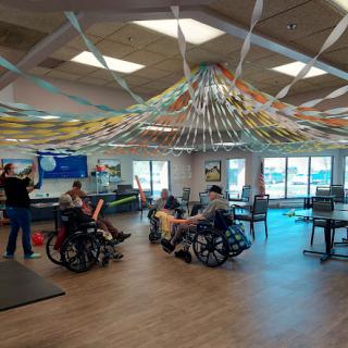 A vibrant activity room filled with colorful streamers and individuals in wheelchairs engaging in social activities.