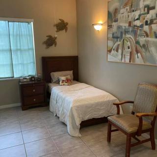 A minimalist bedroom interior featuring a single bed, nightstand, chair, and wall art.
