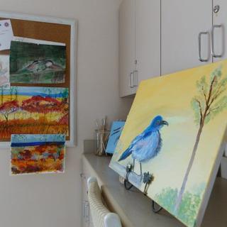 A cozy art studio displaying a painting of a blue bird on a canvas alongside other landscape artworks.