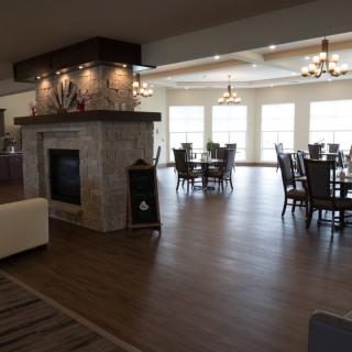 A spacious dining area with a fireplace, hardwood floors, and multiple tables and chairs flooded with natural light from large windows.