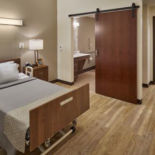 A hospital room featuring a single bed with modern furnishings and a wooden sliding door.