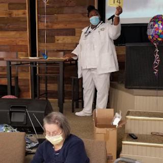 A healthcare worker addresses the audience during a celebration event, emphasizing safety with masks.