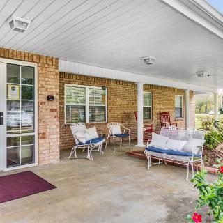 A cozy porch with brick walls, featuring outdoor seating and vibrant flowers.