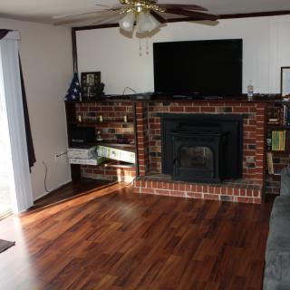 A cozy living room featuring a brick fireplace, mounted television, and wood flooring, complemented by a ceiling fan.