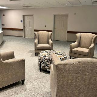 A quiet waiting room with four beige armchairs and a central ottoman.