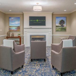 A cozy living room with armchairs arranged around a fireplace, decorated with paintings and a patterned carpet.