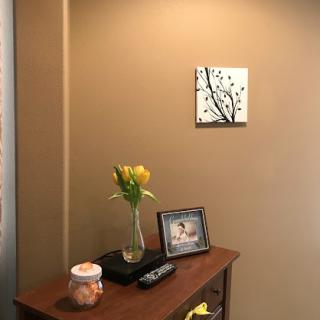 A minimalist interior space featuring a small wooden table with a vase of yellow flowers, a photo frame, and wall art.