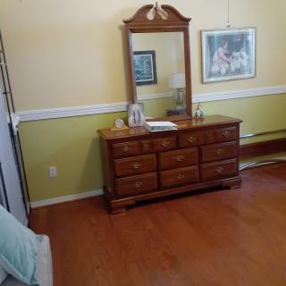 A bedroom with a wooden dresser and mirror, featuring a hardwood floor and a framed painting on the wall.