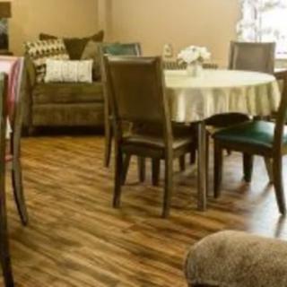 A cozy dining and living area with wooden flooring, featuring a table with chairs and a sofa in the background.