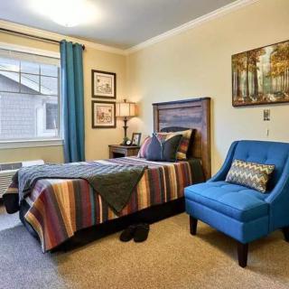 A cozy bedroom with a colorful bedspread, blue accent chair, and decorative artwork.