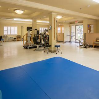 A spacious rehabilitation gym equipped with exercise machines and a blue mat for therapy activities.