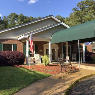A building entrance with a green awning, seating area, and flag.