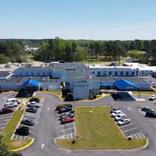 Aerial view of a healthcare facility with a large parking lot and blue canopies.