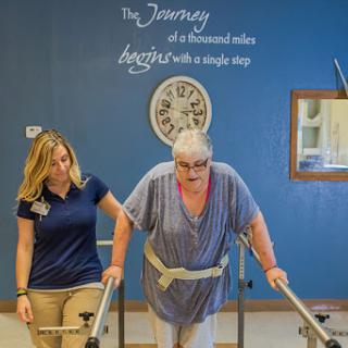 A patient receives support while practicing walking with the help of a therapist in a rehabilitation setting.