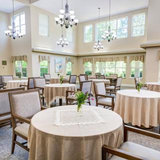 A bright dining room with elegantly set round tables, chairs, and large windows.