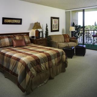 A cozy bedroom with a bed and sofa, featuring warm decor and a large window.