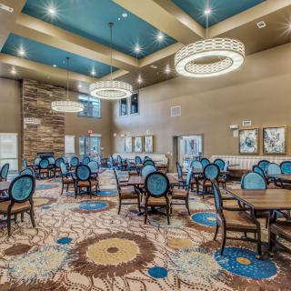 A spacious and elegantly decorated dining area with chandeliers, featuring multiple tables and chairs on a patterned carpet.