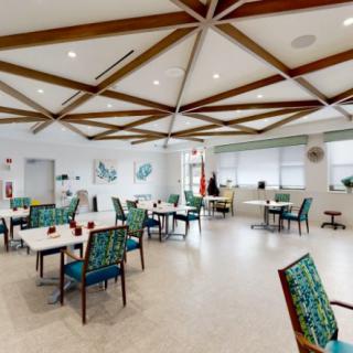A modern dining area with stylish chairs and tables, accented by wooden ceiling beams and ample natural lighting.