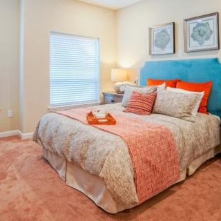A cozy bedroom with a colorful headboard and decorative pillows, featuring wall art and a soft carpet.