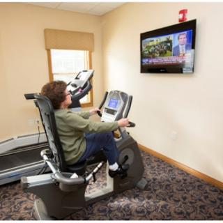 A person exercising on a recumbent bike in a fitness room while watching television.