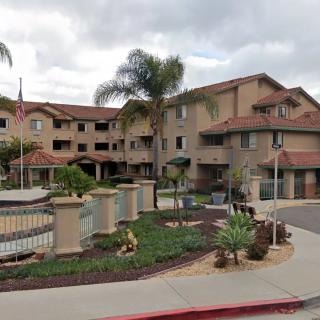 A residential apartment complex with palm trees and well-maintained landscaping under a cloudy sky.