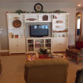 A cozy living room featuring a white entertainment center with a television and decorative shelves, surrounded by comfortable seating.