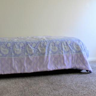 A minimalist bedroom with a bed covered by a patterned blanket on a carpeted floor.