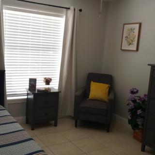 A cozy bedroom corner with a chair, pillow, and a small table by the window.