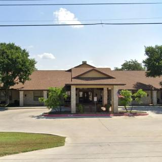 A single-story building with a driveway and trees surrounding it under a clear sky.
