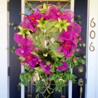 A vibrant wreath adorned with pink and green flowers hanging on a front door.