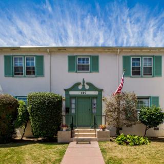 A two-story residential building with green shutters and a front entryway, displaying an American flag.