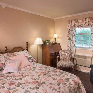 A vintage-style bedroom featuring floral patterns on the bedspread and curtains, with a wooden desk and cozy lighting.