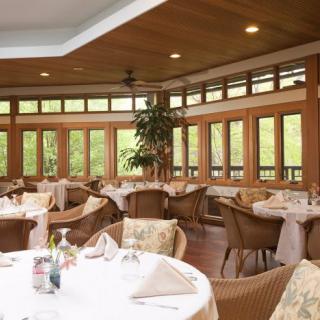 A cozy dining area with tables and wicker chairs, surrounded by large windows.