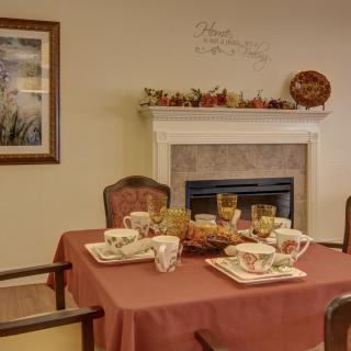 A cozy dining area with a table set for a meal, featuring autumn-themed decorations and a fireplace.