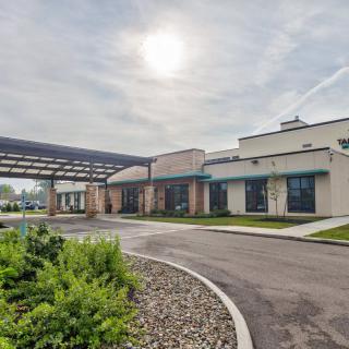 Modern building with a covered driveway and landscaped surroundings on a sunny day.