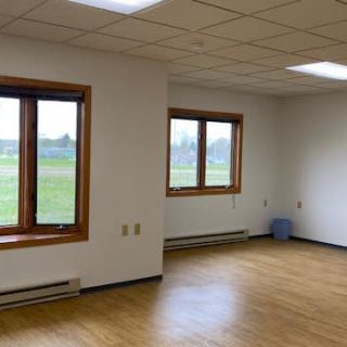 An empty room with wooden floors and large windows allowing natural light in.