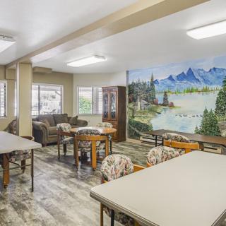 A spacious room with tables, chairs, and couches, featuring a scenic mural on the wall.