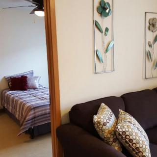 A cozy living room with a view into the bedroom, decorated with floral wall art and accent pillows.