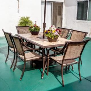 A patio set with a table and six chairs, adorned with potted plants, placed on an outdoor deck.