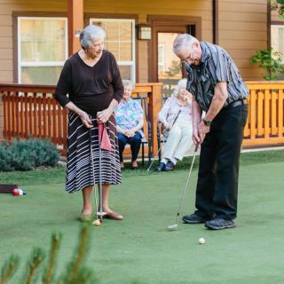 An elderly couple enjoying a game of golf on a putting green.