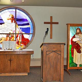 An interior view of a church featuring a pulpit, altar, and stained glass windows.