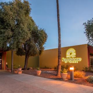 A modern building illuminated in the evening, featuring inviting landscaping and a prominent sign.