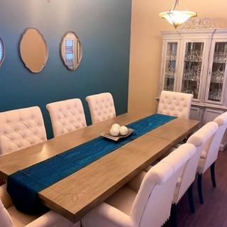 A modern dining room with a sleek wooden table, white upholstered chairs, and a blue accent wall adorned with mirrors.