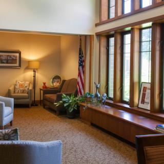 A comfortable office interior with seating, an American flag, and large windows letting in natural light.